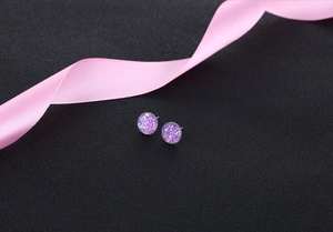 Macro shot of purple crystal cluster stud earrings on black texture with pink ribbon