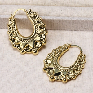Detalle de pendientes en U dorados con patrones en relieve sobre tela beige texturizada