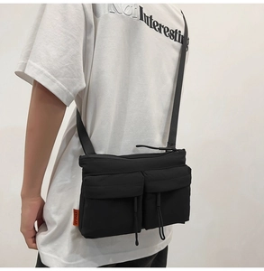 Detail view of a black nylon messenger bag with orange label worn by a model