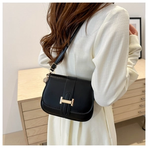 Detail shot of a black PU leather crossbody bag with a gold metal H-shaped buckle on a model