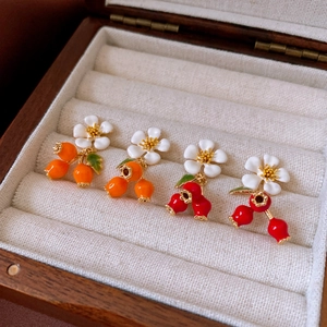 Close-up of white flower earrings with orange and red fruit pendants in a wooden jewelry box