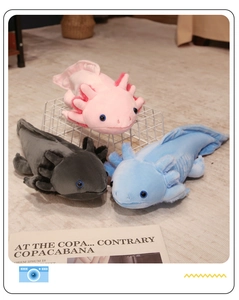 Three colorful plush axolotl toys in pink, blue, and grey on a cozy soft carpet