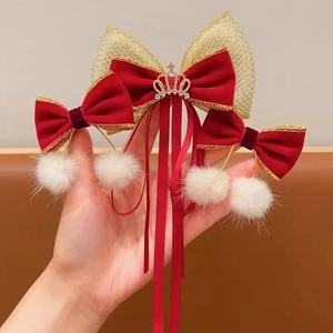 Detailed set of red velvet hair clips with gold crown and white pom-poms shown by hand