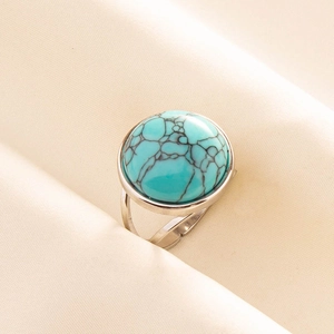 Detail of adjustable silver ring with round turquoise stone on soft fabric background