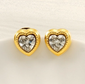 Macro shot of gold heart stud earrings with bezel-set zirconia and milgrain edge