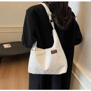 Detailed side view of white canvas tote bag with brown leather logo and adjustable strap