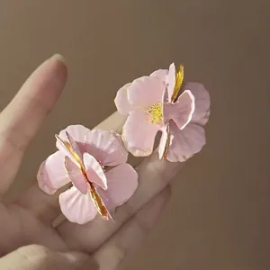 Detail of pink flower stud earrings with enamel petals and gold edges held in hand