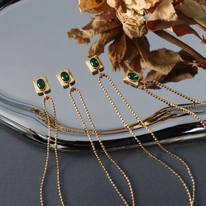 Vintage gold necklaces with square emerald pendants on a reflective metallic tray