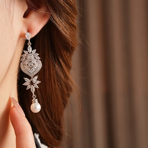 Macro detail of leaf-shaped earring with sparkling zircons and a heart pearl drop