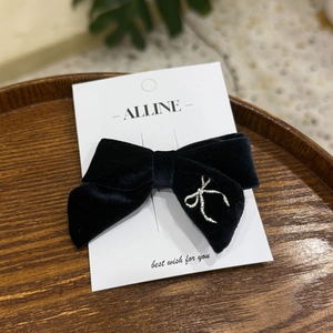 Elegant black velvet bow hair clip with silver embroidery on a rustic wooden plate
