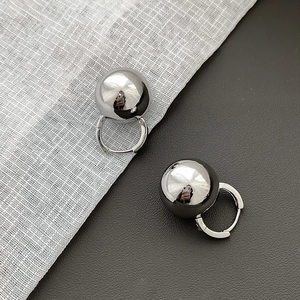 Detailed view of shiny silver spherical earrings on textured fabric and leather background