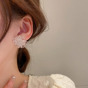 Close-up of a white resin flower stud earring worn by a model in soft warm lighting