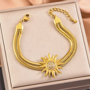 Macro view of a gold double snake chain bracelet with sparkling sun charm on silk