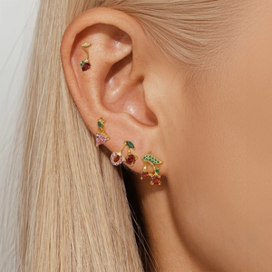 Close-up of gold cherry stud earrings with pink and red gems on a model's ear