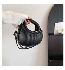 Detail of black pleated crescent handbag with vertical ribbed texture and gold metal zipper