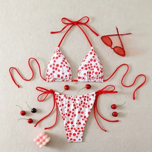 Detailed flat lay of white cherry print bikini set with red side ties and bow accents