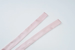 Detail view of smooth light pink satin ribbons with silky texture on white background
