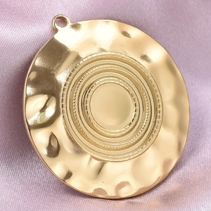 Macro shot of gold stainless steel round pendant with hammer texture on purple silk