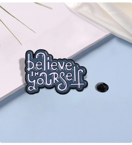 Detail of metal pin showing 'believe in yourself' lettering with black butterfly clutch
