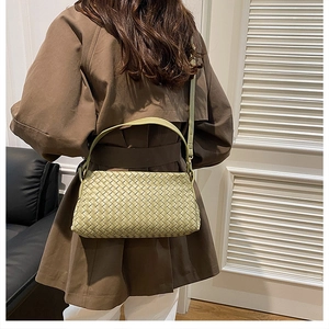Détail du sac à bandoulière en cuir tressé vert porté par un mannequin en trench