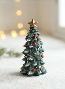 Close-up of green resin mini Christmas tree with snow effect and red bow ornaments