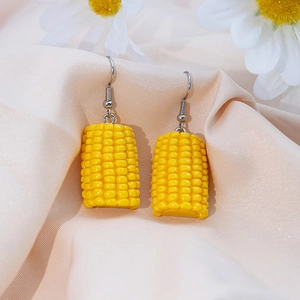 Macro shot of realistic yellow resin corn earrings on a beige silk fabric background