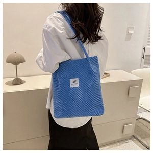 Detail of blue corduroy tote bag featuring 'You need this one' label worn by a model