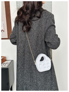 Detail of white PVC mini bag with sculptural design and gold chain strap on grey tweed coat