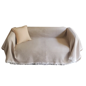 Beige waffle weave sofa cover with decorative tassels on a modern couch with pillow