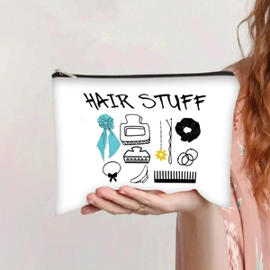 Detail of white canvas zipper pouch featuring black HAIR STUFF text and hair accessory prints