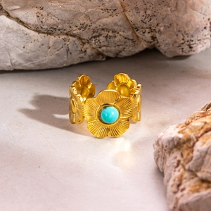 Gros plan détaillé d'une bague florale dorée avec pierre turquoise sur fond de pierre