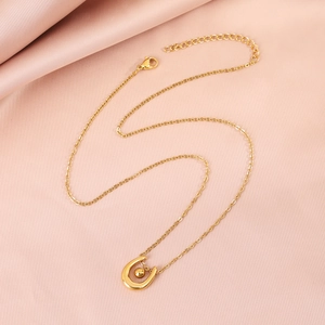 Detail of gold U-shaped horseshoe pendant on cross chain over pink silk background