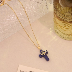 Detail view of a blue natural stone cross pendant with a gold plane and colorful gems
