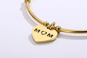 Gros plan d'un pendentif cœur doré avec gravure MOM sur un bracelet en acier poli