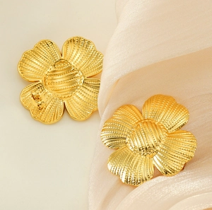 Close-up of golden textured flower stud earrings on beige silk fabric background