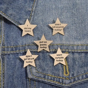 Set of 5 gold star-shaped enamel pins with funny phrases on blue denim jacket