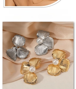Detailed view of gold and silver floral pearl earrings on elegant champagne silk fabric
