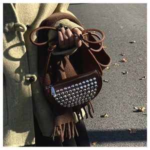 Detail of brown half-moon bag featuring silver studs and a braided leather strap