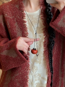 Close-up of vintage handmade persimmon pendant necklace worn on a textured sweater