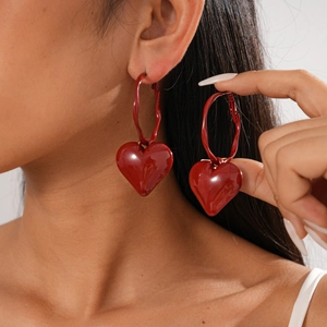 Detail of a red heart-shaped hoop earring featuring a glossy 3D pendant on model