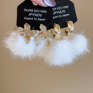 Detailed macro view of white faux fur pompom earrings with gold flower zircon studs