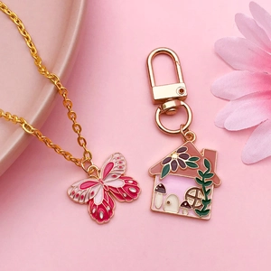Colorful enamel butterfly necklace and mushroom house keychain set on pink background