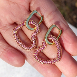 Dettaglio di orecchini a cuore placcati oro 18K con zircone rosa tenuti in una mano