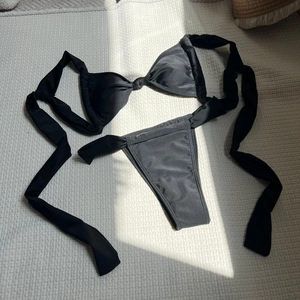 Flat lay of black triangle bikini top with knot detail and side-tie bottoms on textured fabric