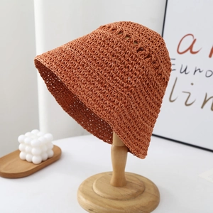 Detailed close-up of handmade crochet straw bucket hat in caramel orange on wooden stand