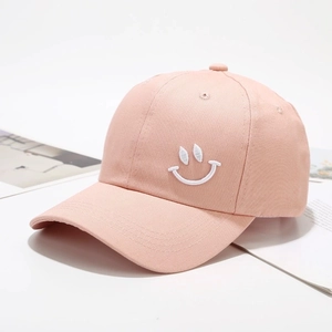 Detailopname van het witte geborduurde smiley-logo op de lichtroze katoenen baseballpet