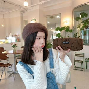Brown corduroy pencil case with cartoon bear pattern held by hand in a cozy cafe setting