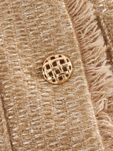 Nahaufnahme eines goldenen gewebten Knopfes und schimmernder Tweed-Struktur einer Jacke