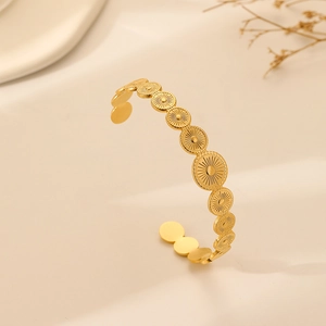 Detail of gold open bangle featuring solar sunburst relief and polished metal texture