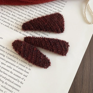 Detailed view of three burgundy plush hair clips set on vintage book pages with pearls
